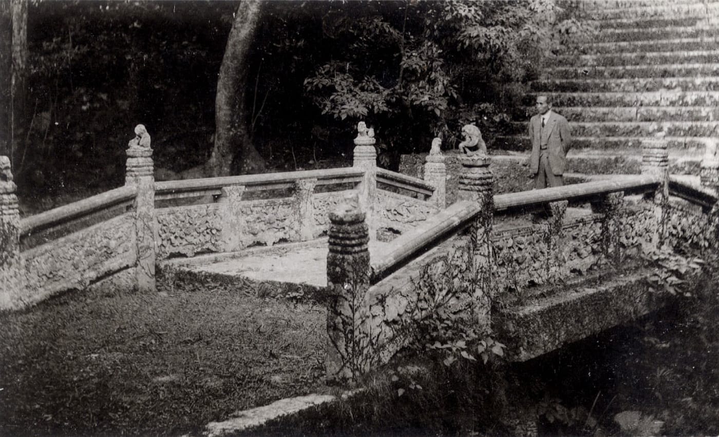A pre-war black-and-white photograph of the carved stone bridge at Enkaku-ji temple in Naha, Okinawa, with a man in a suit beside the balustrade.