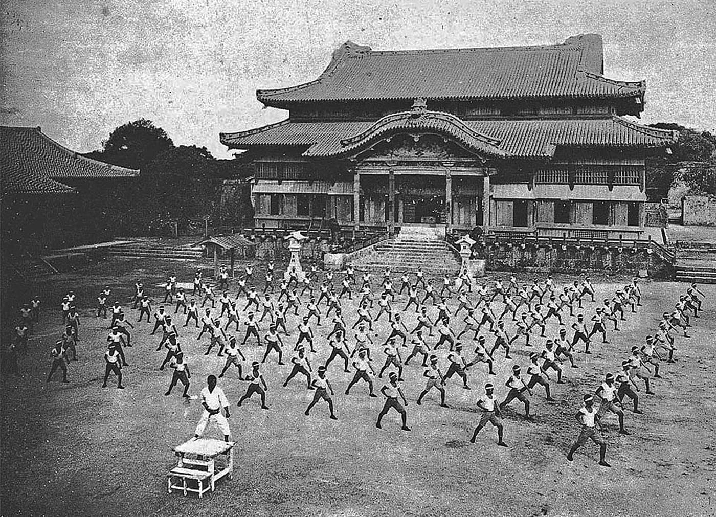 A 1938 black-and-white photograph of karate practitioners training in front of Shuri Castle, Okinawa.