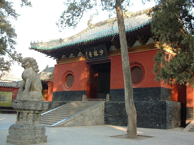 A colour photograph of a hall at the Shaolin Monastery with a stone lion in the foreground.